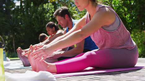 Vielfältige-Männliche-Und-Weibliche-Gruppe-Praktiziert-Yoga-Stretching,-Sitzt-Auf-Matten-Im-Sonnigen-Park