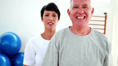 Fisioterapeuta-Sonriente-Ayudando-A-Un-Paciente-Anciano-A-Levantar-Pesas-En-Las-Manos