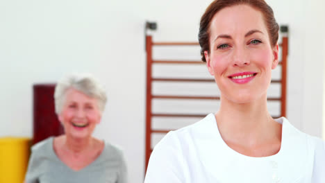 Physical-therapist-smiling-at-camera-with-patient-dancing-in-background