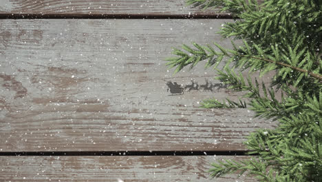 Tree-branches-and-santa-claus-in-sleigh-being-pulled-by-reindeers-against-wooden-plank