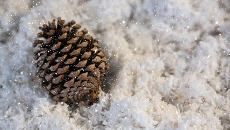 Snow-falling-over-pine-cone-on-snow-on-wooden-surface