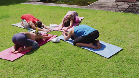 Diverse-group-practicing-yoga,-kneeling-on-mats-and-stretching-in-sunny-park