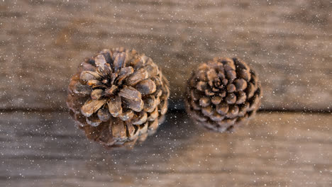 Snow-falling-over-two-pine-cones-on-wooden-surface