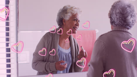 Animation-of-pink-hearts-over-happy-caucasian-senior-woman-putting-on-lipstick-at-home