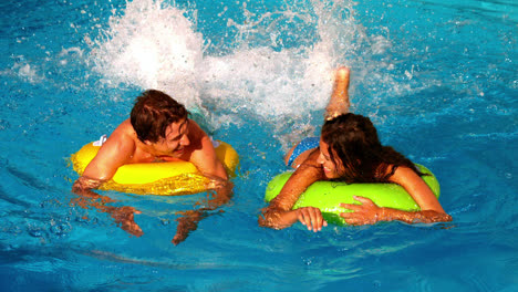 Young-couple-splashing-and-having-fun-in-swimming-pool-on-inflatable-rings