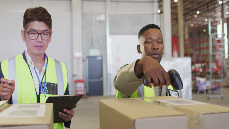 Diverse-male-workers-wearing-safety-suits-and-scanning-boxes-in-warehouse