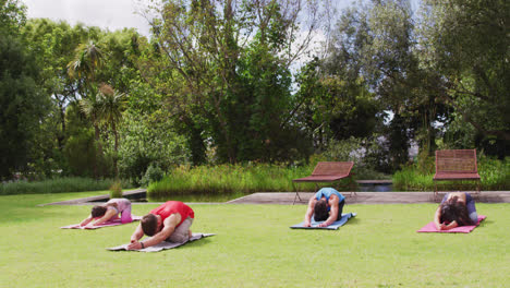 Diverse-group-of-men-and-women-practicing-yoga-kneeling-on-mats-in-park