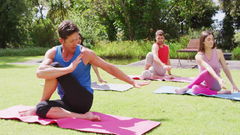 Grupo-Diverso-De-Hombres-Y-Mujeres-Practicando-Yoga-Sentados-En-Esteras-En-El-Parque-Soleado