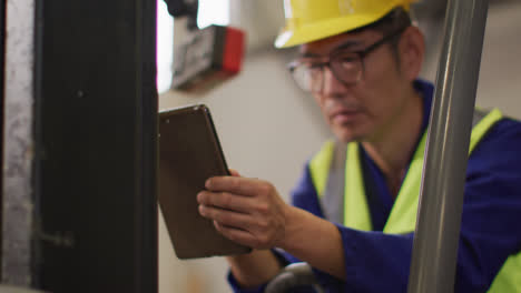 Asian-male-worker-wearing-safety-suit-with-helmet-using-tablet-in-warehouse