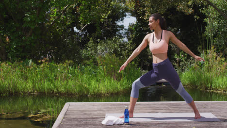 Asiatische-Frau-Praktiziert-Yoga-Pose-Auf-Holzsteg-Durch-Fluss-Und-Wald