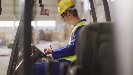 Asian-male-worker-wearing-safety-suit-with-helmet-talking-in-warehouse