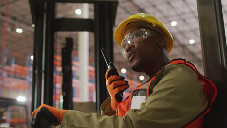 African-american-male-worker-wearing-safety-suit-with-helmet-talking-in-warehouse