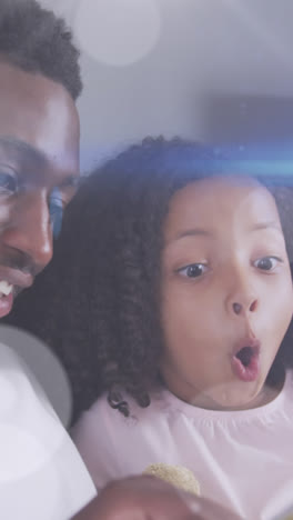 Animation-of-light-spots-over-happy-african-american-father-reading-book-with-daughter