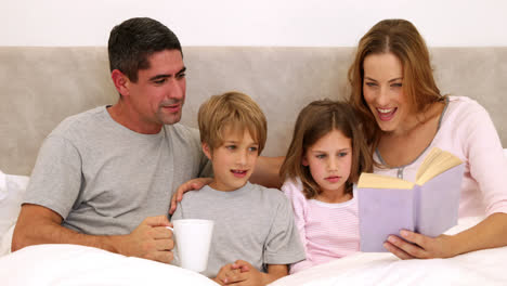 Lächelnde-Eltern-Und-Kinder-Lesen-Zusammen-Im-Bett