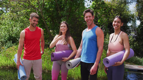 Portrait-of-smiling-diverse-group-with-rolled-up-mats-gathering-for-outdoor-yoga-class