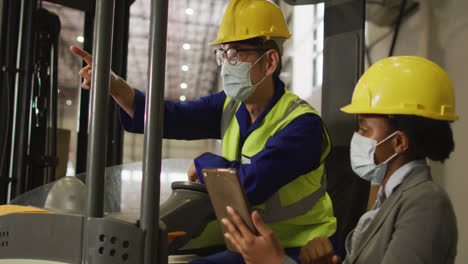 Diverse-male-and-female-workers-wearing-face-masks-and-using-tablet-in-warehouse