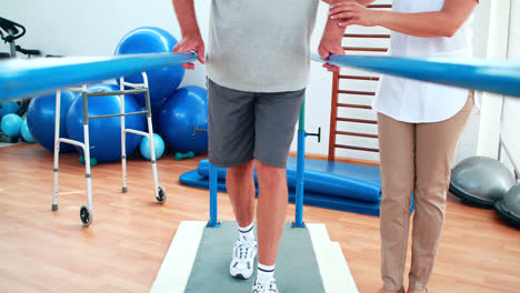 Physiotherapist-helping-patient-walk-with-parallel-bars