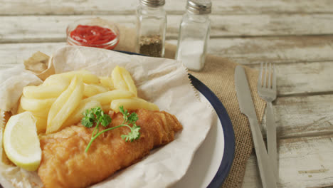 Video-of-fish-and-chips-on-plate,-salt-and-pepper-and-ketchup-on-wooden-table