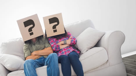 Kaukasisches-Paar-Sitzt-Auf-Der-Couch-Mit-Kartons-Mit-Fragezeichen-über-Dem-Kopf