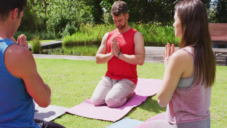 Happy-diverse-group-practicing-yoga-pose-kneeling-on-mats-in-sunny-park