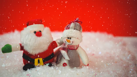 Schnee-Fällt-über-Weihnachtsmann-Und-Schneemann-Spielzeug-Vor-Rotem-Hintergrund