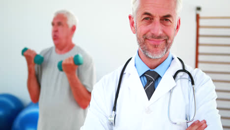 Smiling-doctor-looking-at-camera-with-patient-exercising-in-background