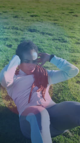 Spots-of-light-against-african-american-fit-woman-performing-crunches-on-the-grass