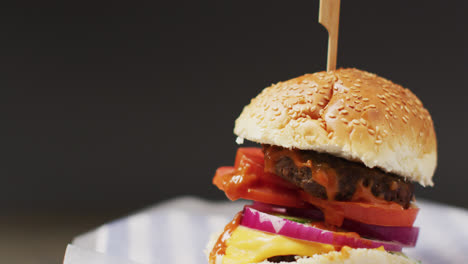 Video-close-up-of-cheeseburger-in-burger-bun-with-wooden-skewer,-on-grey-background-with-copy-space