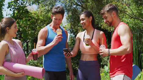 Happy-diverse-group-of-men-and-women-with-health-drinks-laughing-after-yoga-class-in-sunny-park
