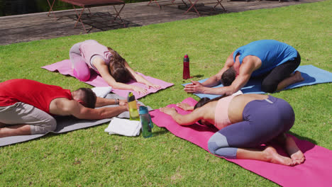 Grupo-Diverso-Practicando-Yoga,-Arrodillándose-Sobre-Colchonetas-Y-Estirándose-En-Un-Parque-Soleado