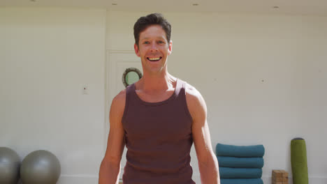 Portrait-of-smiling-caucasian-male-yoga-instructor-in-sunny-fitness-studio
