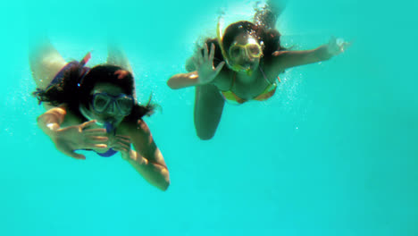 Happy-friends-waving-at-camera-underwater-wearing-snorkels