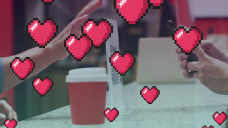 Multiple-pink-heart-icons-floating-against-a-person-making-payment-through-smartphone-at-a-cafe