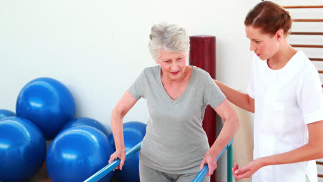 Smiling-physical-therapist-helping-patient-walk-with-parallel-bars