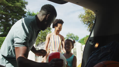 Glückliche-Afroamerikanische-Familie-Packt-Auto-Mit-Wasserbällen-Im-Urlaub
