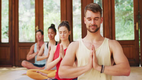 Grupo-Diverso-Sonriente-Sentado-En-Posición-De-Yoga-Con-Los-Ojos-Cerrados,-Durante-La-Clase-De-Yoga-En-El-Estudio