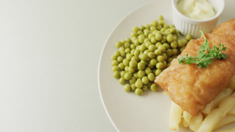 Video-of-fish,-chips-and-peas-on-plate-with-dip,-with-copy-space-on-white-background