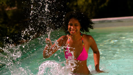 Happy-woman-in-pink-bikini-splashing-at-camera-in-swimming-pool