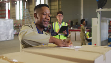 Diverse-male-workers-with-clipboard-and-boxes-smiling-in-warehouse