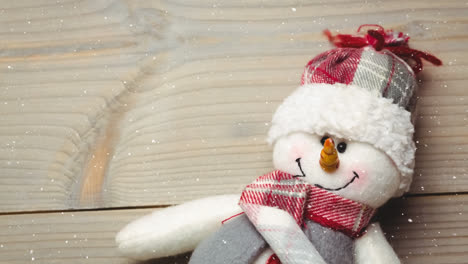 Snow-falling-over-close-up-of-snowman-toy-on-wooden-surface