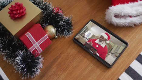 African-american-man-wearing-santa-costume-on-christmas-video-call-on-tablet