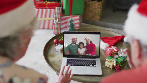 Senior-caucasian-couple-using-laptop-for-christmas-video-call-with-happy-family-on-screen