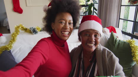 Feliz-Madre-Afroamericana-E-Hija-Adulta-Con-Sombreros-De-Santa-En-Videollamada-Navideña,-Cámara-Lenta