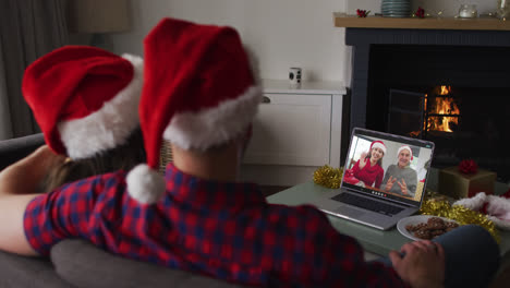 Caucasian-couple-on-laptop-video-call-with-senior-couple-at-christmas-time