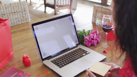 Happy-biracial-woman-with-gifts-making-valentine's-day-laptop-video-call,-with-copy-space-on-screen