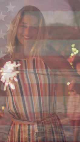 Animation-of-flag-of-united-states-of-america-over-happy-diverse-friends-with-sparklers-on-beach