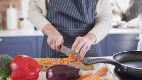 Mid-section-of-woman-wearing-apron-chopping-vegetables-in-the-kitchen-at-home