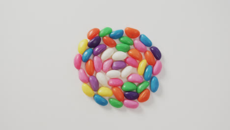 Video-of-overhead-view-of-multi-coloured-sweets-forming-circle-over-white-background