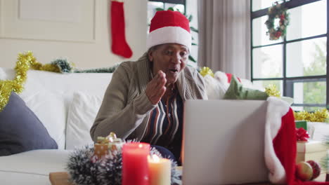 Feliz-Mujer-Mayor-Afroamericana-Con-Sombrero-Navideño-De-Papá-Noel-Haciendo-Videollamadas-Con-Laptop,-Cámara-Lenta