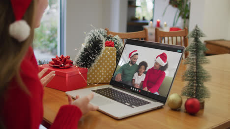 Caucasian-woman-on-laptop-video-call-with-happy-family-at-christmas-time